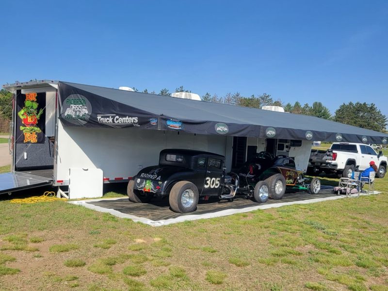 Anderson Oasis Racing trailer awning shading two hot rods on the grass