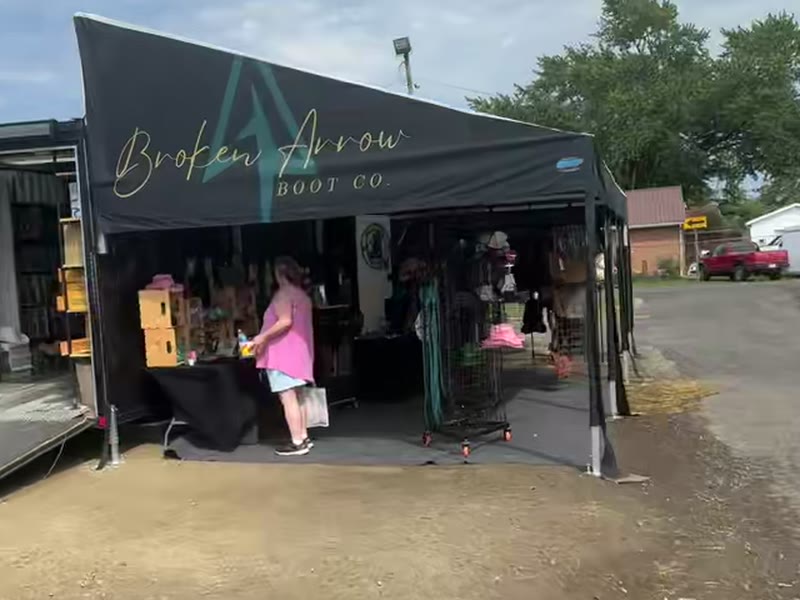 Broken Arrow Boot Co. mobile retail trailer with a black DMP awning printed with their gold logo, open for business at an event