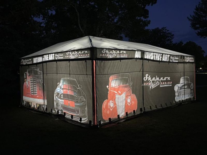 Shannon Watts Art mobile sales enclosure lit from inside at night, its printed classic car graphics glowing